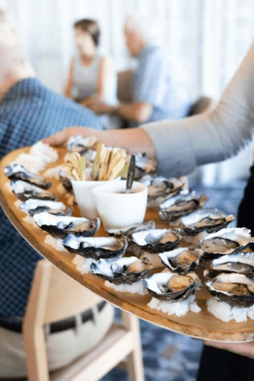 Hand holding a serving platter of oysters at a VIP event.