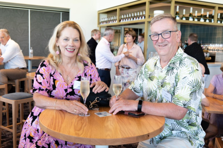 Resident in pink floral dress with champagne and man in green button-up shirt with a wine at Pacific Golf Club's new Clubhouse.